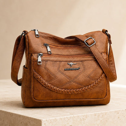 Tan leather crossbody bag with braided front, two zip compartments, adjustable strap