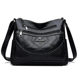 Black leather crossbody bag front with braided panel, zip top, and brand logo