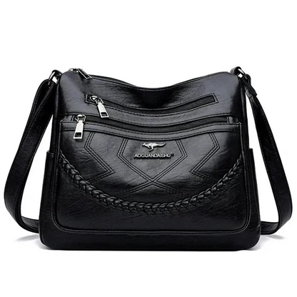 Black leather crossbody bag front with braided panel, zip top, and brand logo