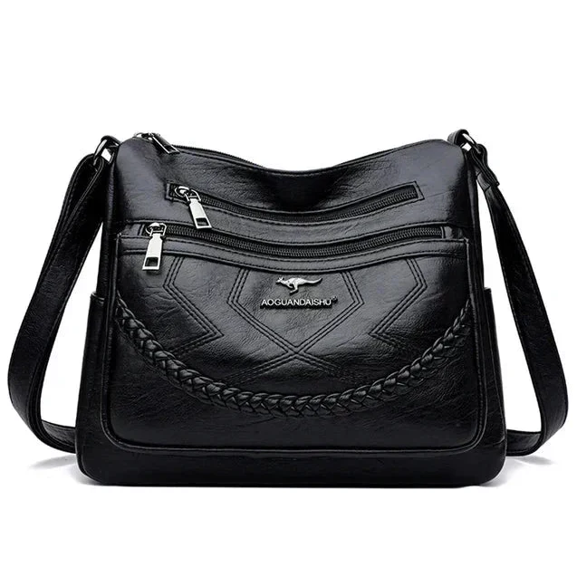 Black leather crossbody bag front with braided panel, zip top, and brand logo