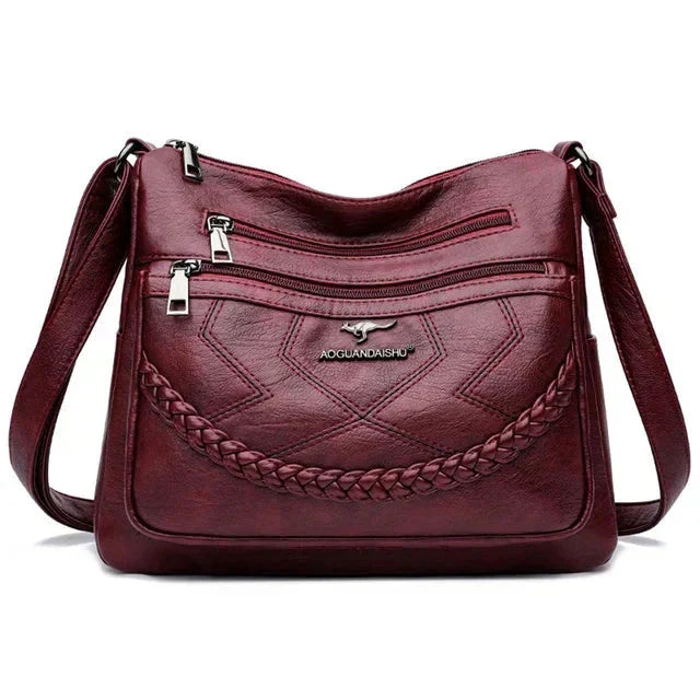Burgundy leather crossbody bag front with braided panel, zip pockets, adjustable strap