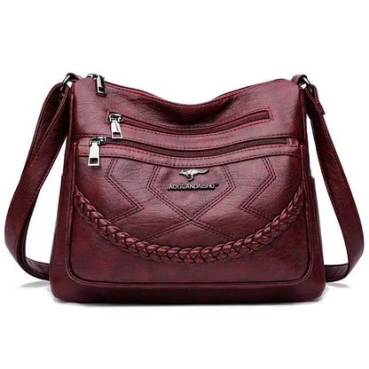 Burgundy leather crossbody bag front with braided panel, zip pockets, adjustable strap
